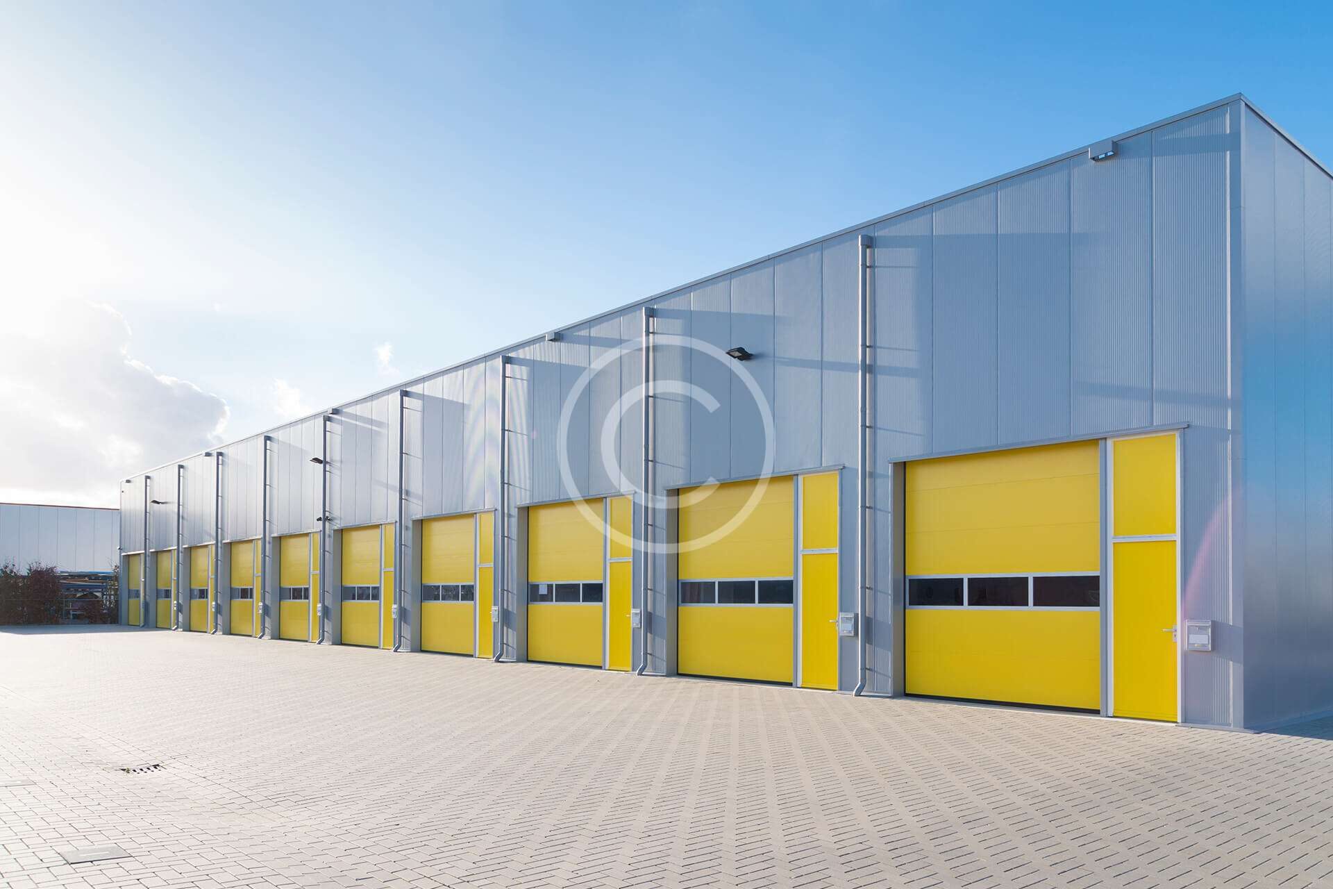 Modern industrial building with yellow loading dock doors under a clear sky.
