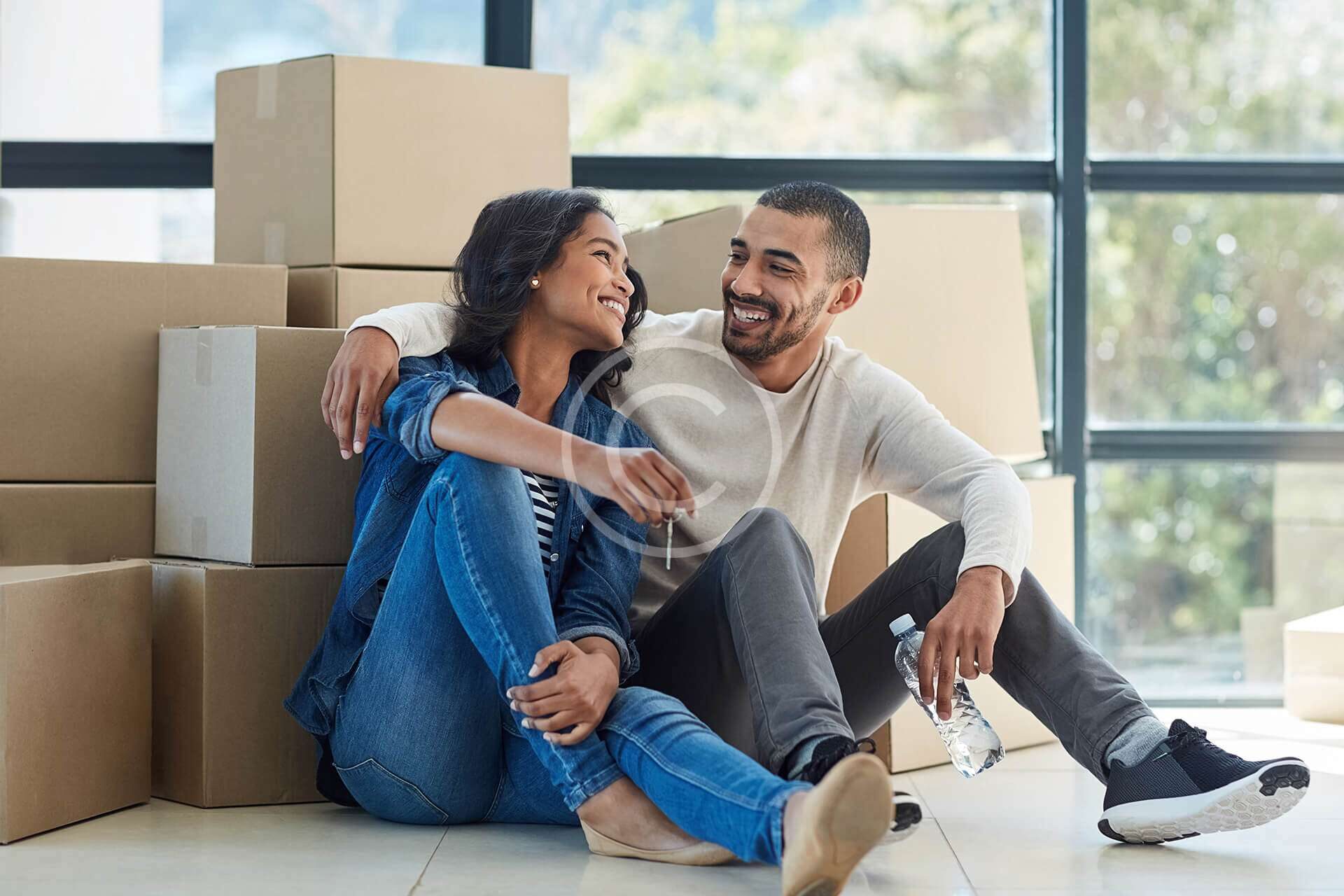 Couple sitting happily on the floor amid moving boxes.