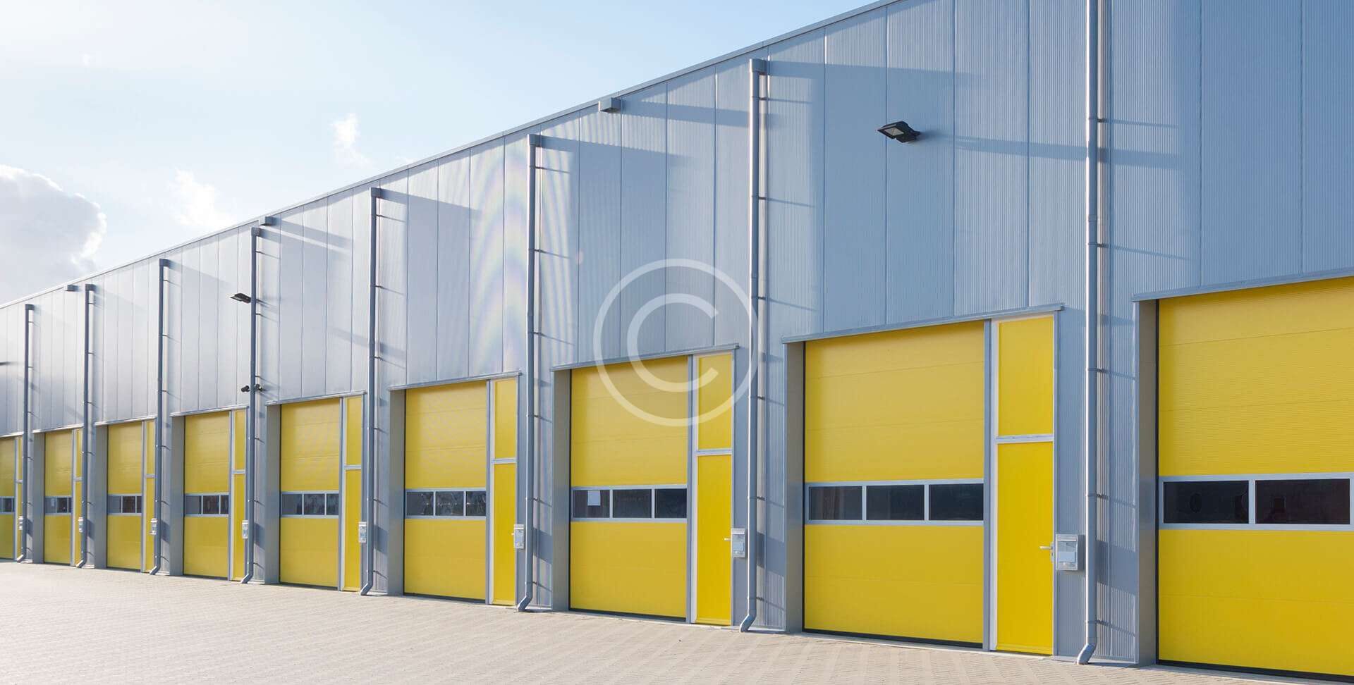 Modern industrial building with yellow garage doors under a clear sky.