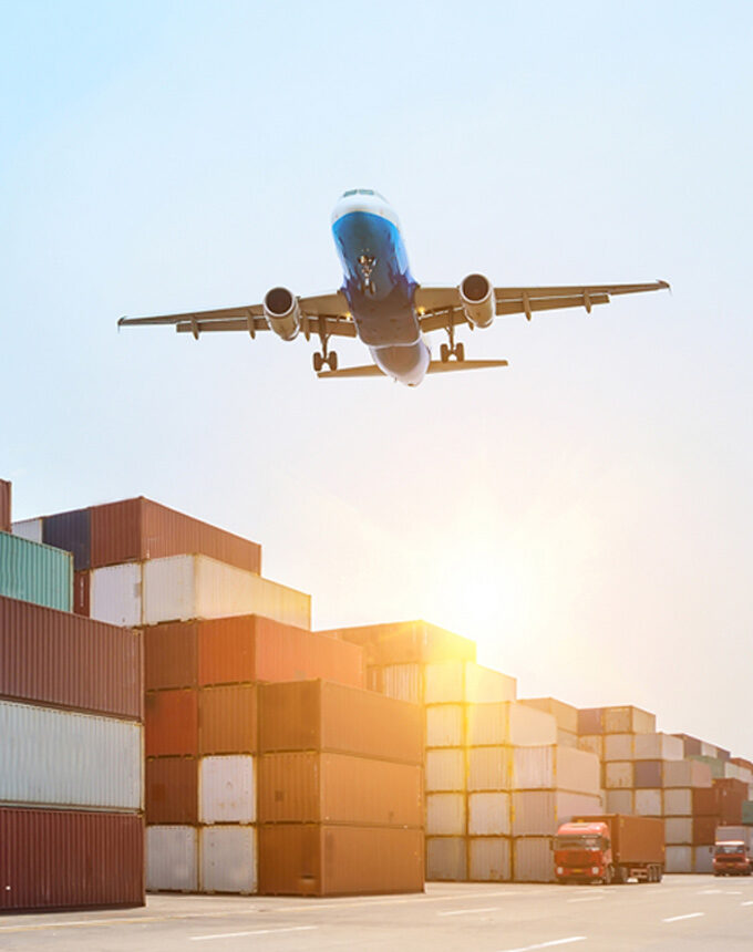Cargo plane flying over shipping containers during sunset.