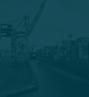 Cargo containers lined up at a busy port with cranes in the background.