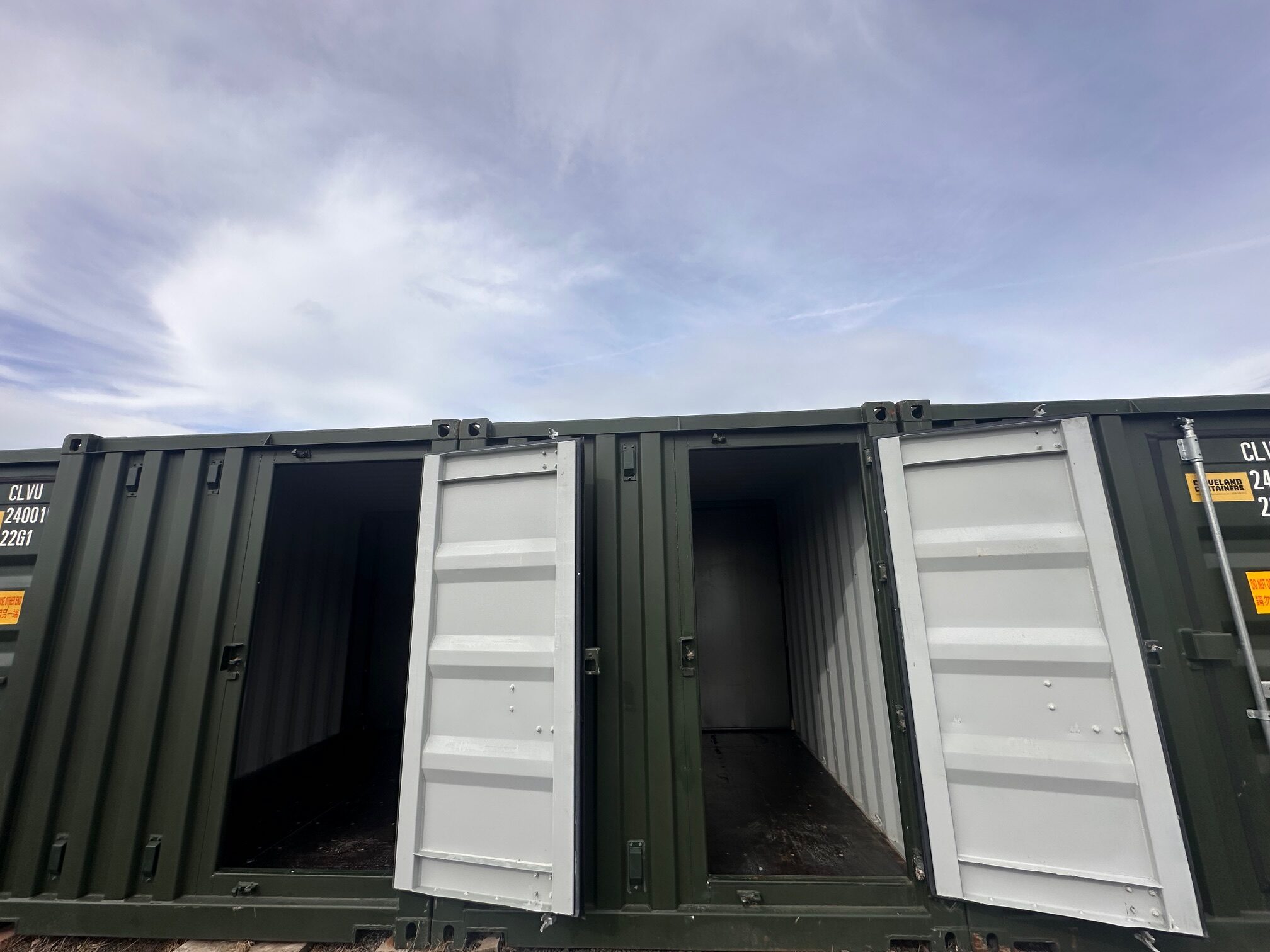 Two open white shipping containers under a cloudy sky.
